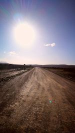 Dirt road amidst field against sky