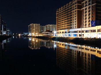 Illuminated buildings by river against sky at night