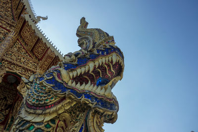 Low angle view of serpent-like creature 'naga' ststue against temple building against clear blue sky