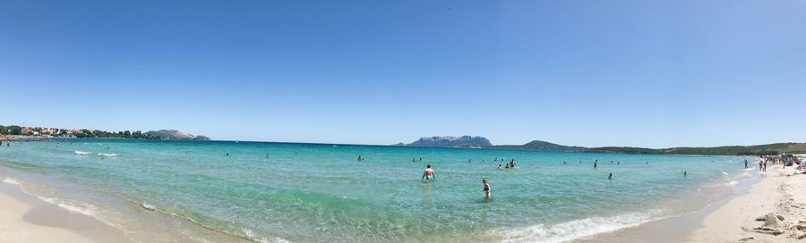 People on beach against clear blue sky