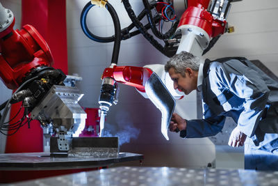 Mature worker with welding helmet working at robotics in factory