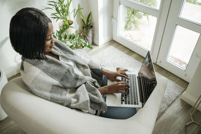 Smiling businesswoman using laptop in armchair at home