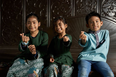 Malay siblings sitting side by side with hand gesture during ramadan festival 