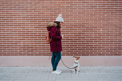 Woman with dog standing on footpath against wall