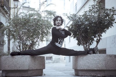 Full length portrait of man with legs apart balancing on retaining walls in city