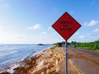 Road sign by sea against sky