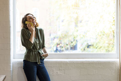 Happy businesswoman talking on smart phone standing by window