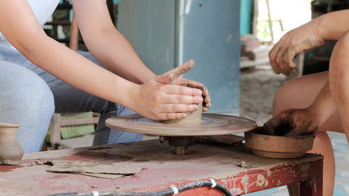 Midsection of people working on pottery wheel at workshop