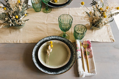 Rustic dining table setting, dried flowers in a vase, green glass glasses and ceramic plates