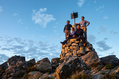 Low angle view of people on rock formation against sky