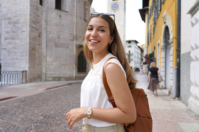 Portrait of smiling young woman standing on street in city