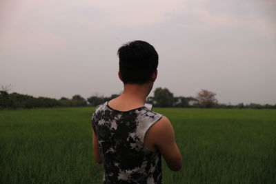 Rear view of man standing on field against sky during sunset