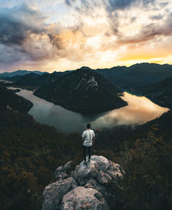 Rear view of man standing on mountain against sky during sunset