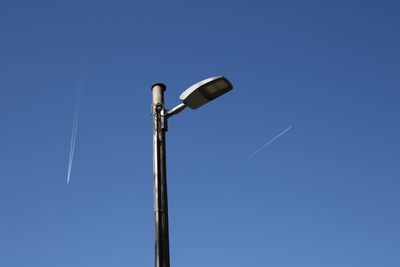 Low angle view of street light with vapor trails in blue sky