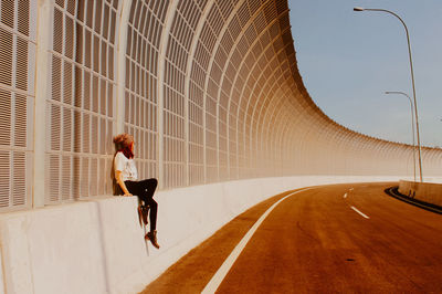 Full length side view of woman sitting on retaining wall in city