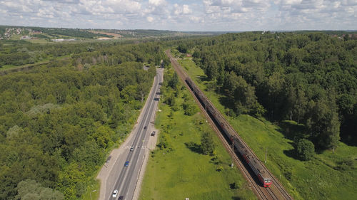 Highway with motor vehicles and a railway with an electric train in the countryside. 