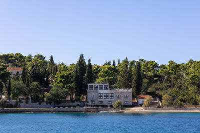 Buildings by river against clear blue sky