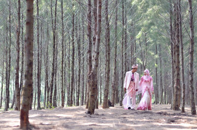 Bride and groom walking amidst trees in forest