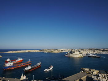 Boats in sea against clear blue sky