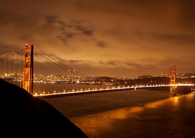 Illuminated san franciscooakland bay bridge over sea against cloudy sky at night