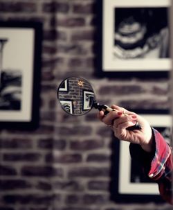 Cropped image of woman holding magnifying glass against wall