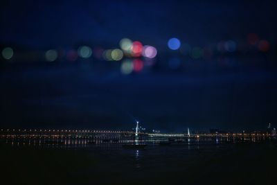 Illuminated city by river against sky at night