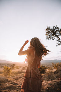 Woman standing on field against clear sky during sunset