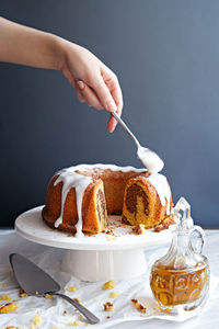 Cropped image of woman hand decorating marble cake with icing against gray background