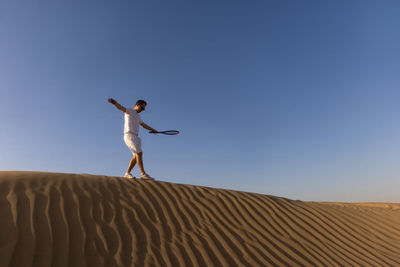 Rear view of woman jumping on sand at desert against clear sky