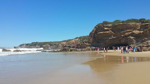 People at beach against clear blue sky