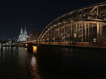 Illuminated bridge over river against buildings at night