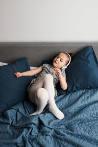 High angle view of girl listening music while lying on bed at home