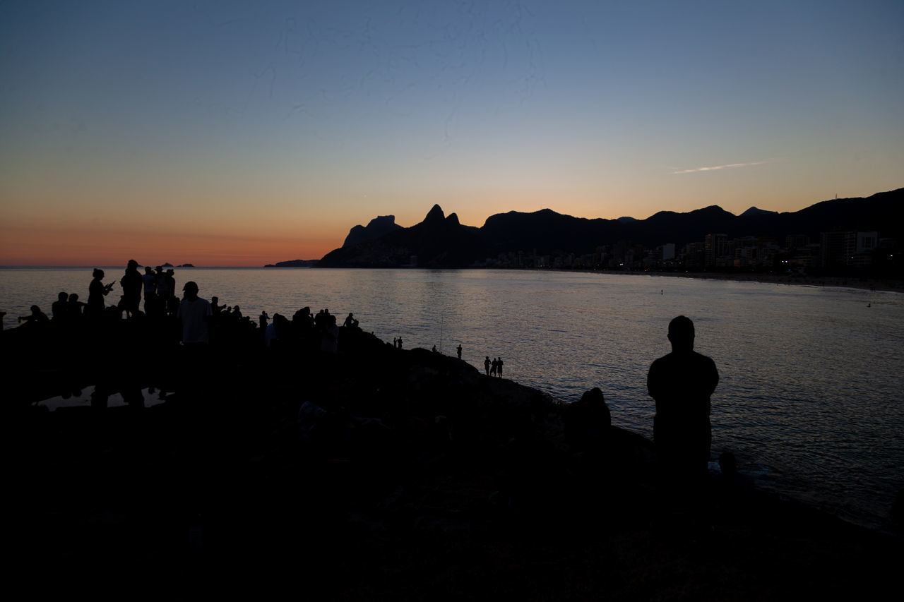 SILHOUETTE PEOPLE SITTING ON SHORE AT SUNSET