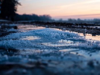 Surface level of frozen land against sky during sunset