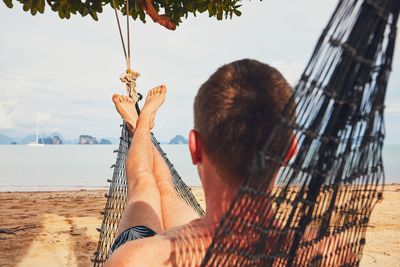 Man relaxing in hammock at beach against sky