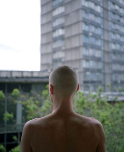 Rear view of shirtless man standing against building in city