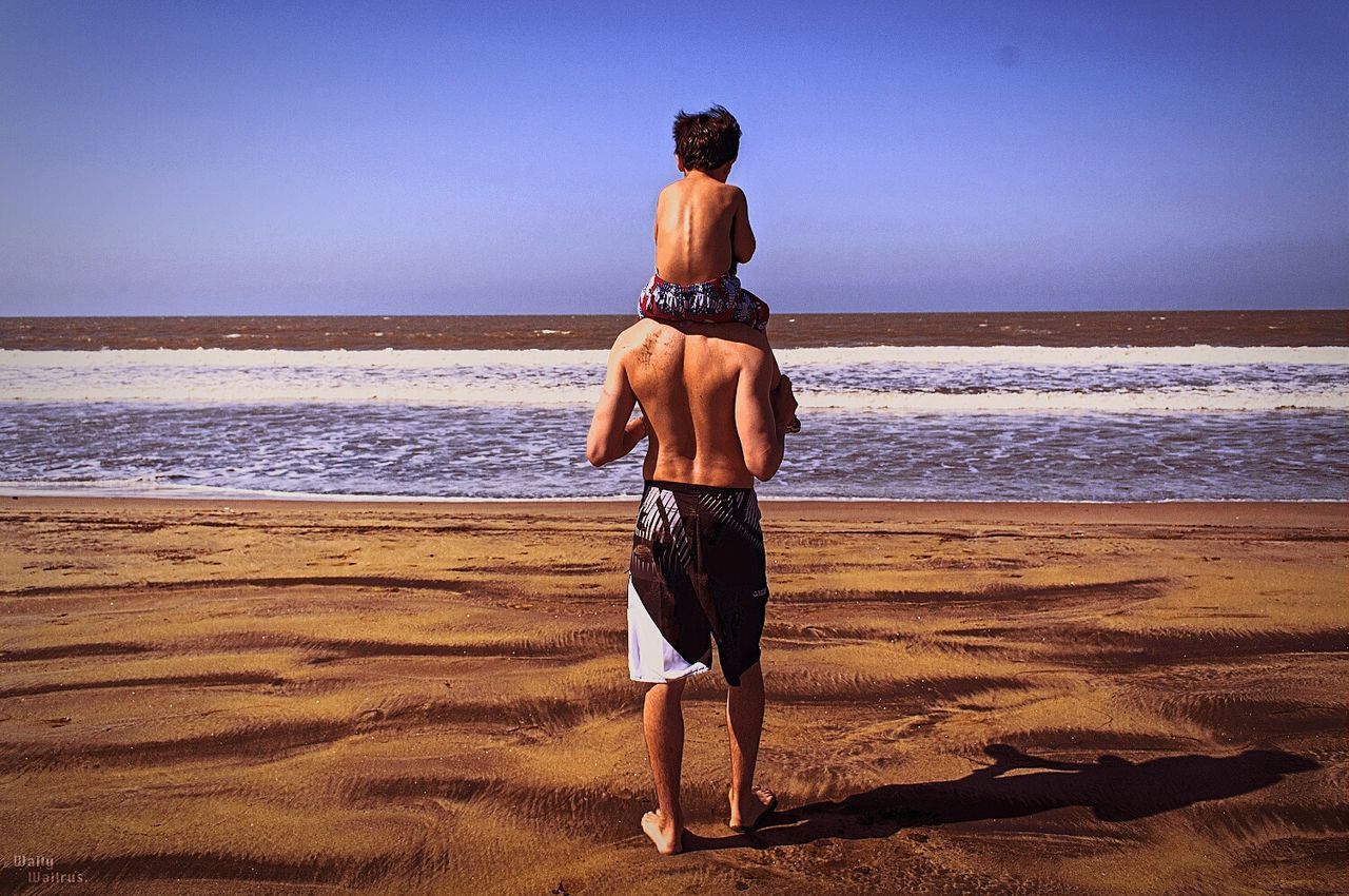 REAR VIEW OF WOMAN STANDING ON BEACH