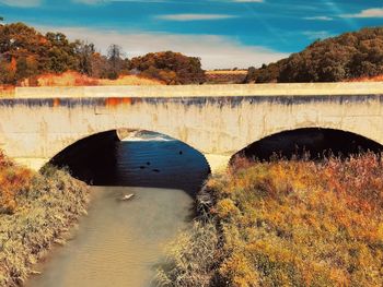 Arch bridge over river against sky during autumn