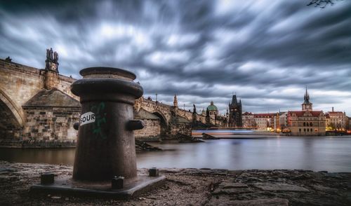View of buildings by river against cloudy sky