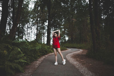 Full length portrait of woman on road amidst trees in forest