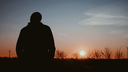 Rear view of silhouette man standing against sky during sunset