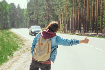 Rear view of backpacker hitchhiking on road in forest