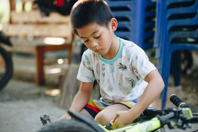 Cute boy repairing bicycle while sitting outdoors