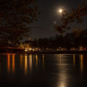 Illuminated city by river against sky at night