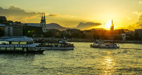 Boats in river with city in background during sunset