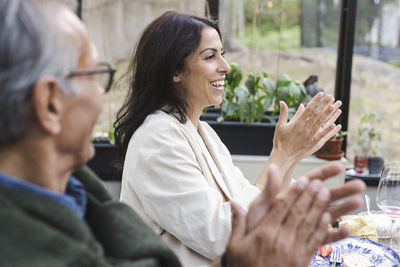 Side view of happy man and woman clapping while sitting at patio during summer party