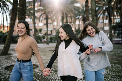 Happy friends standing against trees in city