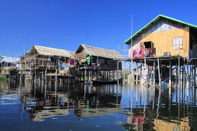 Buildings by lake against clear blue sky