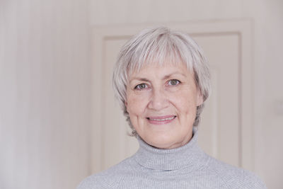 A close-up portrait of a smiling and looking at camera elderly caucasian woman with short gray hair