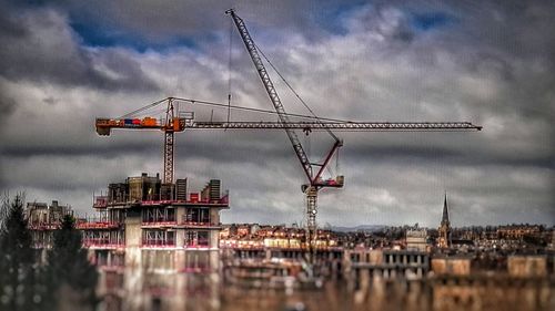 Cranes at construction site against cloudy sky